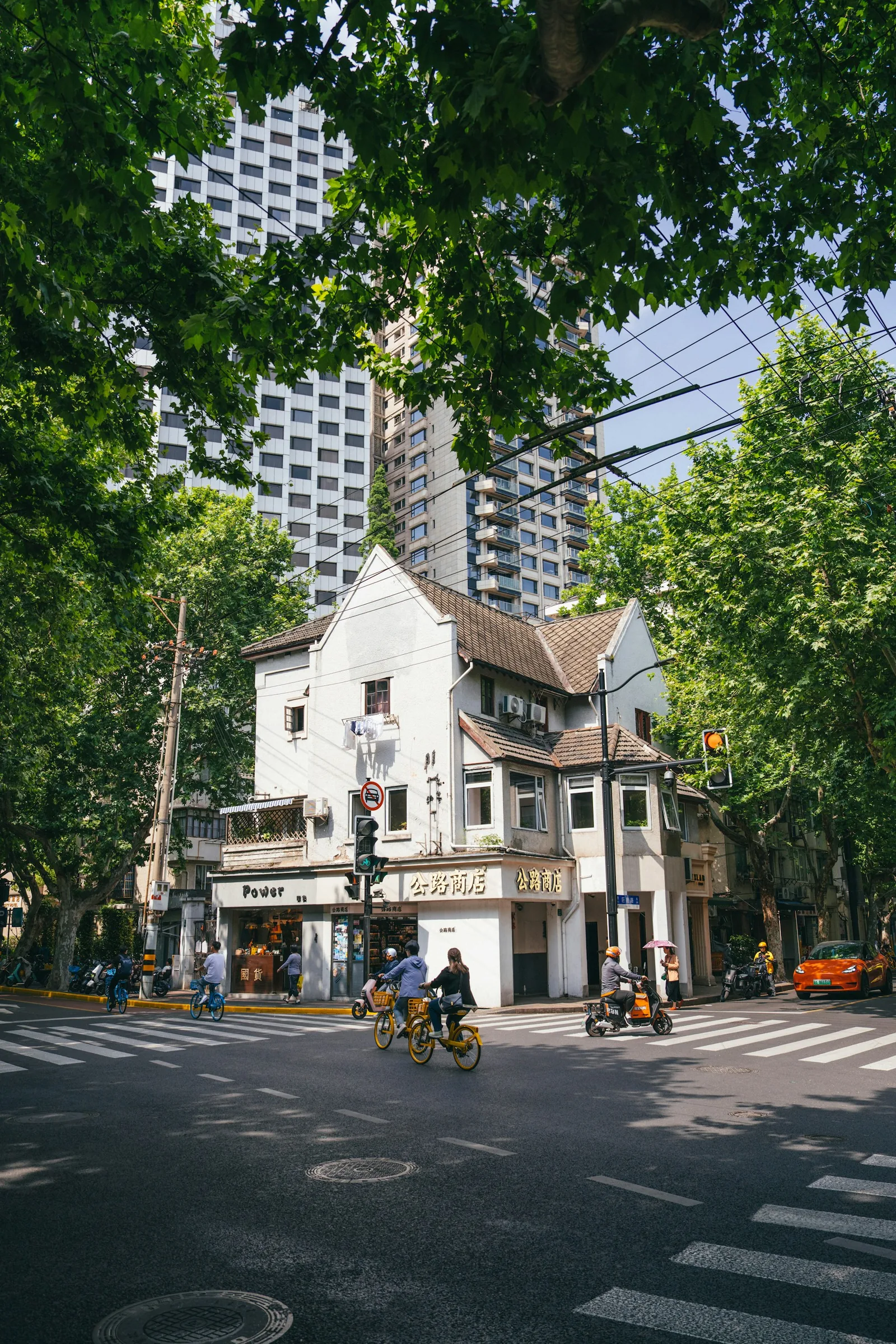 Cyclists and pedestrians passing a leafy historic street corner in Shanghai